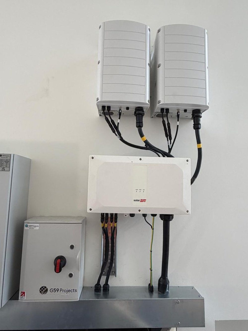 Two SolarEdge inverters mounted above a DC safety unit and AC isolator on a commercial plant room wall